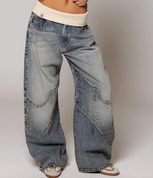 Wide-leg distressed denim jeans with curved stitching, paired with cream ribbed waistband and sandals