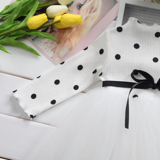 White polka dot tulle dress with black ribbon bow, styled with yellow tulips on white wood