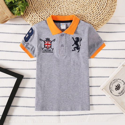Gray kids polo shirt with orange collar, lion and UK flag embroidery, styled on striped fabric