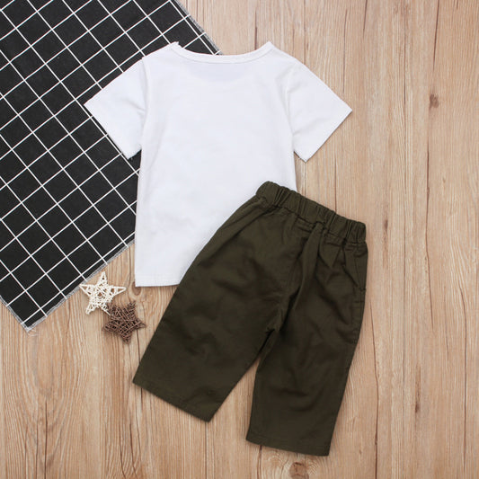 White kids t-shirt with olive green shorts, laid on wood floor beside checkered mat and star decor