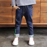 Kids' distressed denim jeans with green lettering, cuffed hems, paired with striped top and white sneakers