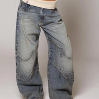 Wide-leg distressed denim jeans with curved stitching, paired with cream ribbed waistband and sandals