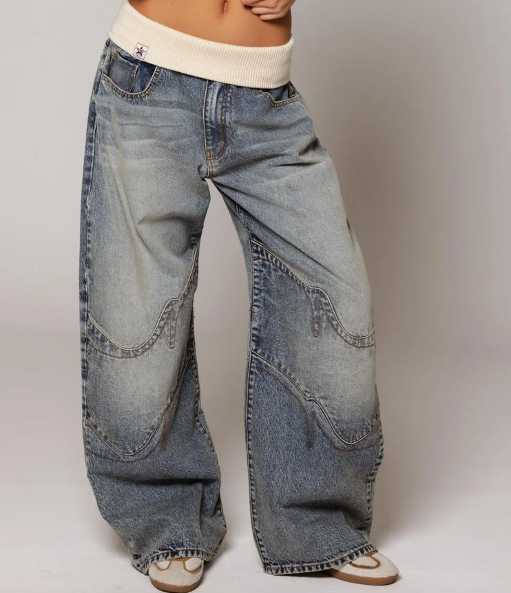 Wide-leg distressed denim jeans with curved stitching, paired with cream ribbed waistband and sandals