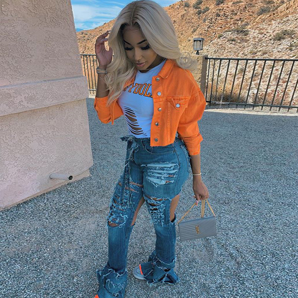 Woman in orange denim jacket, ripped jeans, and white graphic tee, holding gray handbag outdoors