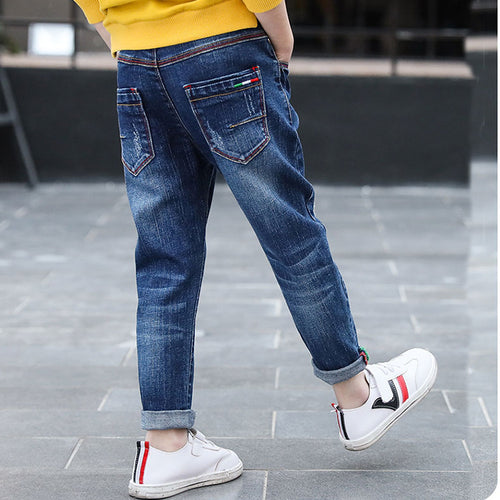 Kids' blue denim jeans with rolled cuffs, colorful stitching, paired with white sneakers and yellow top