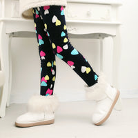 Kids' black leggings with colorful hearts, paired with white fuzzy boots for cozy winter fashion