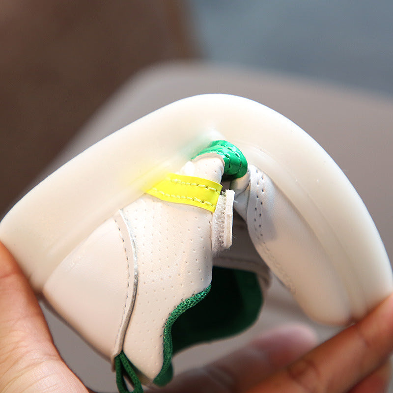 White sneaker with green and yellow accents, held in hand, showcasing perforated design and bold color details