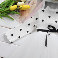 White polka dot tulle dress with black ribbon bow, styled with yellow tulips on white wood