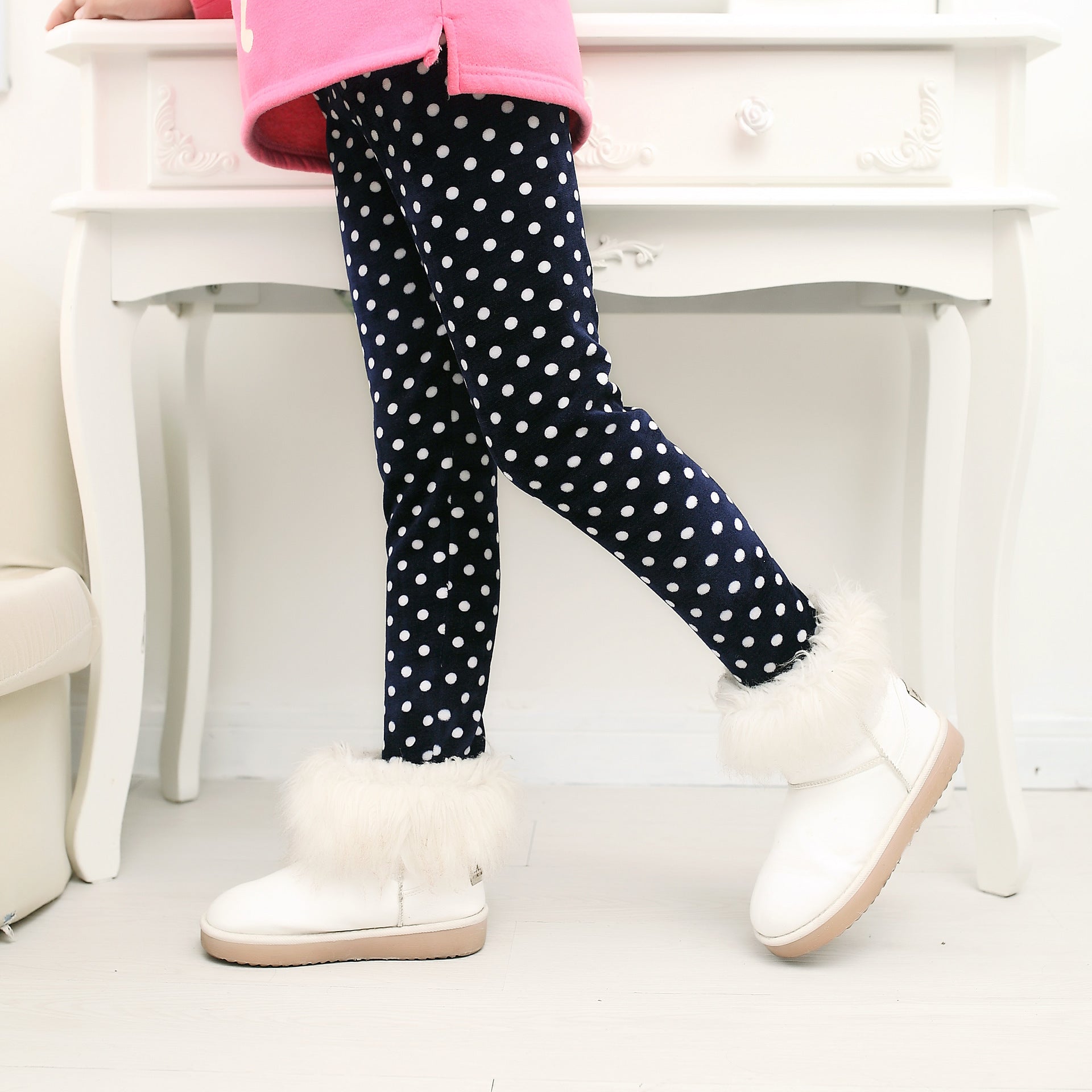 Child wearing navy polka dot leggings with white fur-trimmed boots, cozy winter fashion