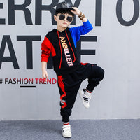 Boy in stylish red and black hoodie set with 'ANBULLET' print, sunglasses, and cap, posing for fashion trend look