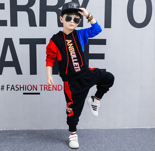 Boy in stylish red and black hoodie set with 'ANBULLET' print, sunglasses, and cap, posing for fashion trend look
