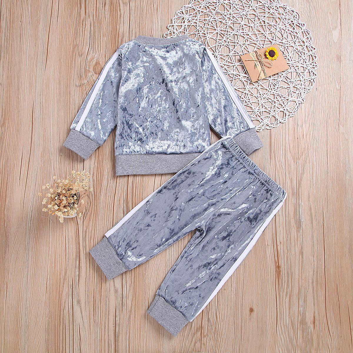Gray crushed velvet kids tracksuit with white side stripes, laid on wooden floor with decorative accents