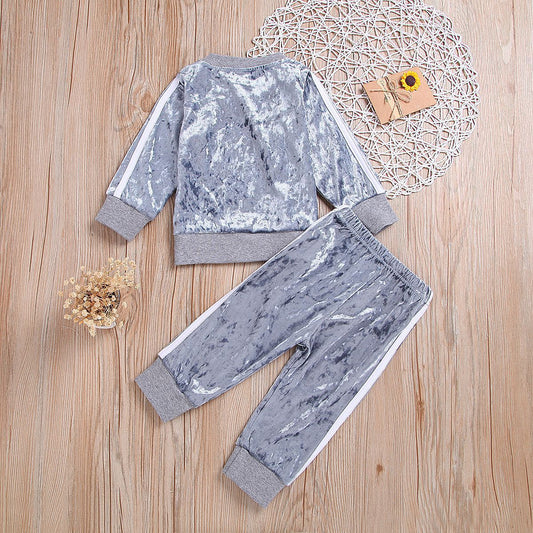 Gray crushed velvet kids tracksuit with white side stripes, laid on wooden floor with decorative accents