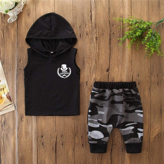 Black sleeveless hoodie with 'Original Gentlemen' print and gray camo pants for kids, laid on wood