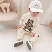 Baby wearing cream Burberry bear print outfit with white cap and sneakers, cozy nursery setting