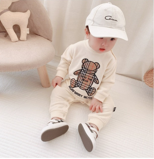 Baby wearing cream Burberry bear print outfit with white cap and sneakers, cozy nursery setting