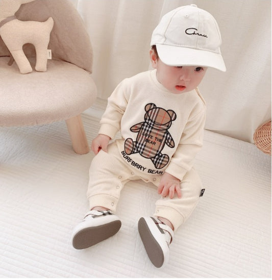 Baby wearing cream Burberry bear print outfit with white cap and sneakers, cozy nursery setting