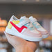 Colorful toddler sneakers with velcro straps, pastel pink, red, yellow, and mint accents, held in hand