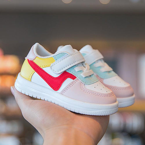Colorful toddler sneakers with velcro straps, pastel pink, red, yellow, and mint accents, held in hand