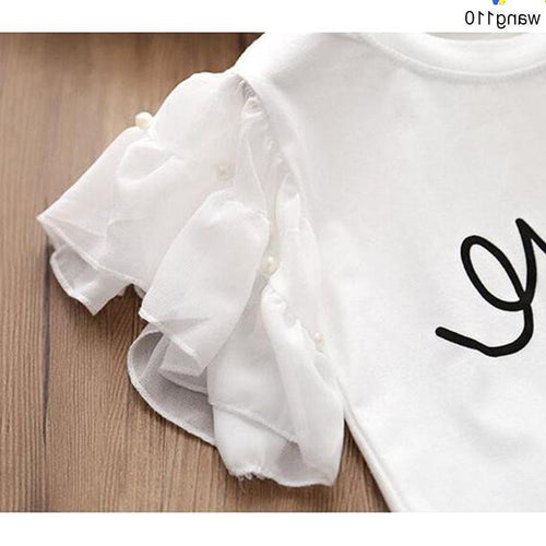 White ruffle sleeve t-shirt with pearl buttons and black script design, laid on wood surface
