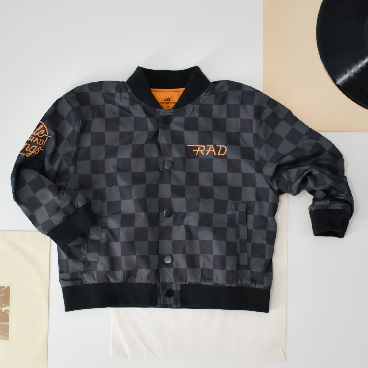 Kids waterproof letterman jacket with checkered pattern by Little Rad Things, featuring a stylish and durable outer layer for outdoor wear.