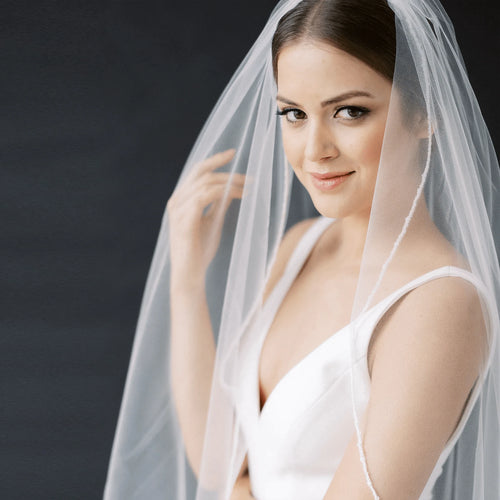 Long flowing wedding veil by MANDOTOS with delicate lace edging and sheer tulle fabric, designed for elegant bridal looks.