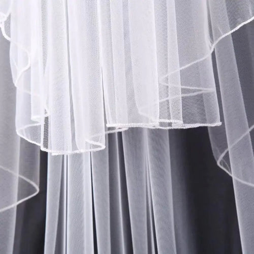 Ethereal double-tiered veil by MANDOTOS featuring delicate lace and flowing tulle for a romantic bridal look.