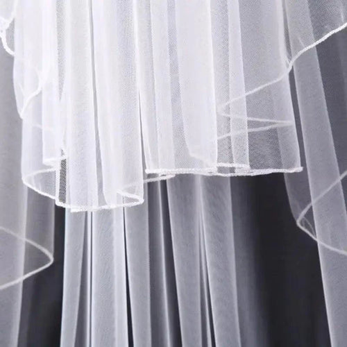 Ethereal double-tiered veil by MANDOTOS featuring delicate lace and sheer fabric, perfect for bridal or special occasion wear.