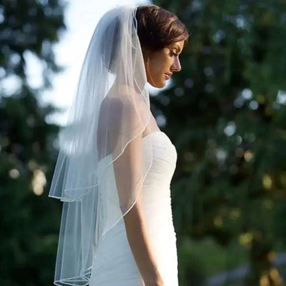 Ethereal double-tiered wedding veil by MANDOTOS with delicate lace edging and soft tulle layers, displayed on a dress form.
